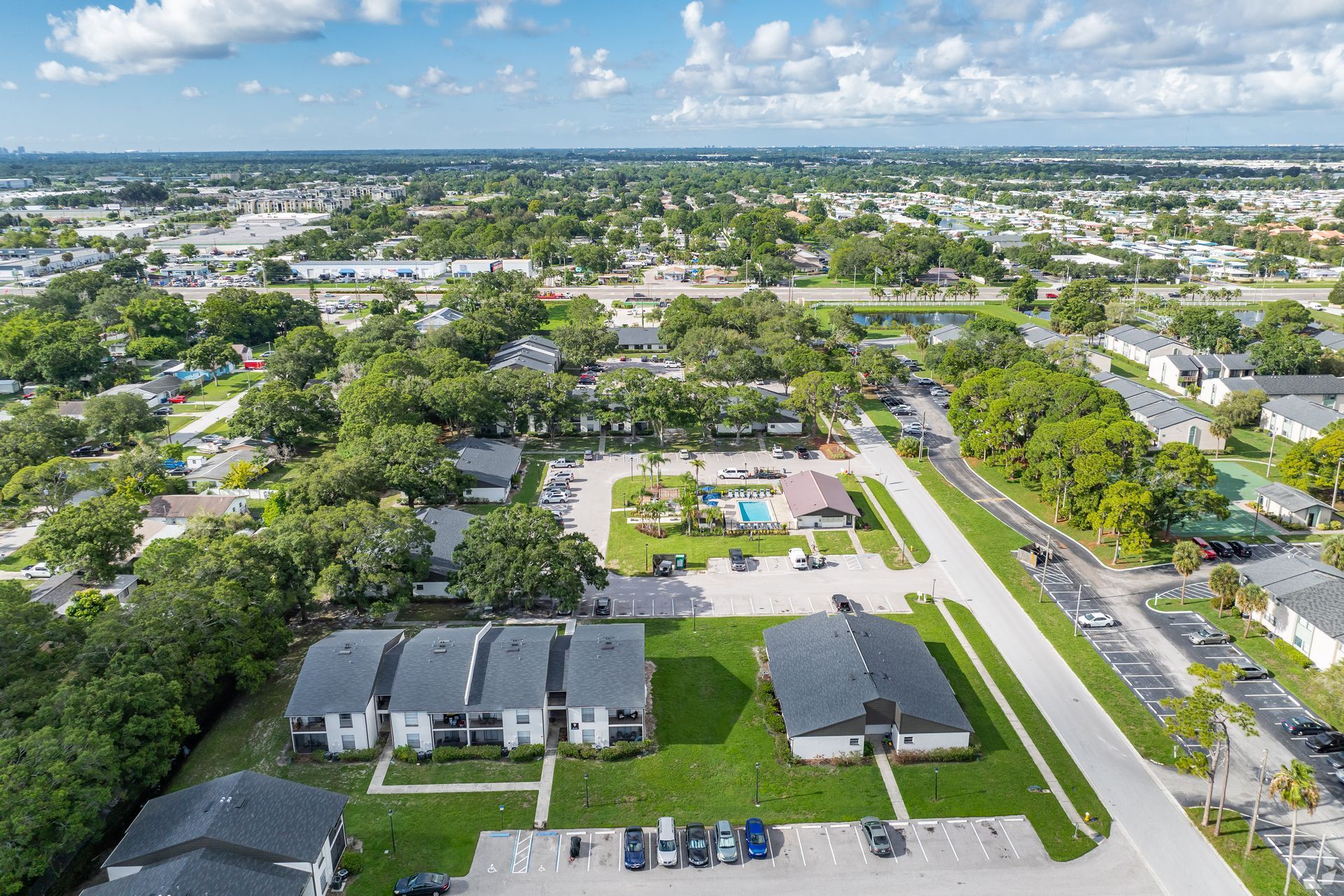 Aerial view of a suburban neighborhood with houses, trees, roads, and a distant city skyline under a blue sky