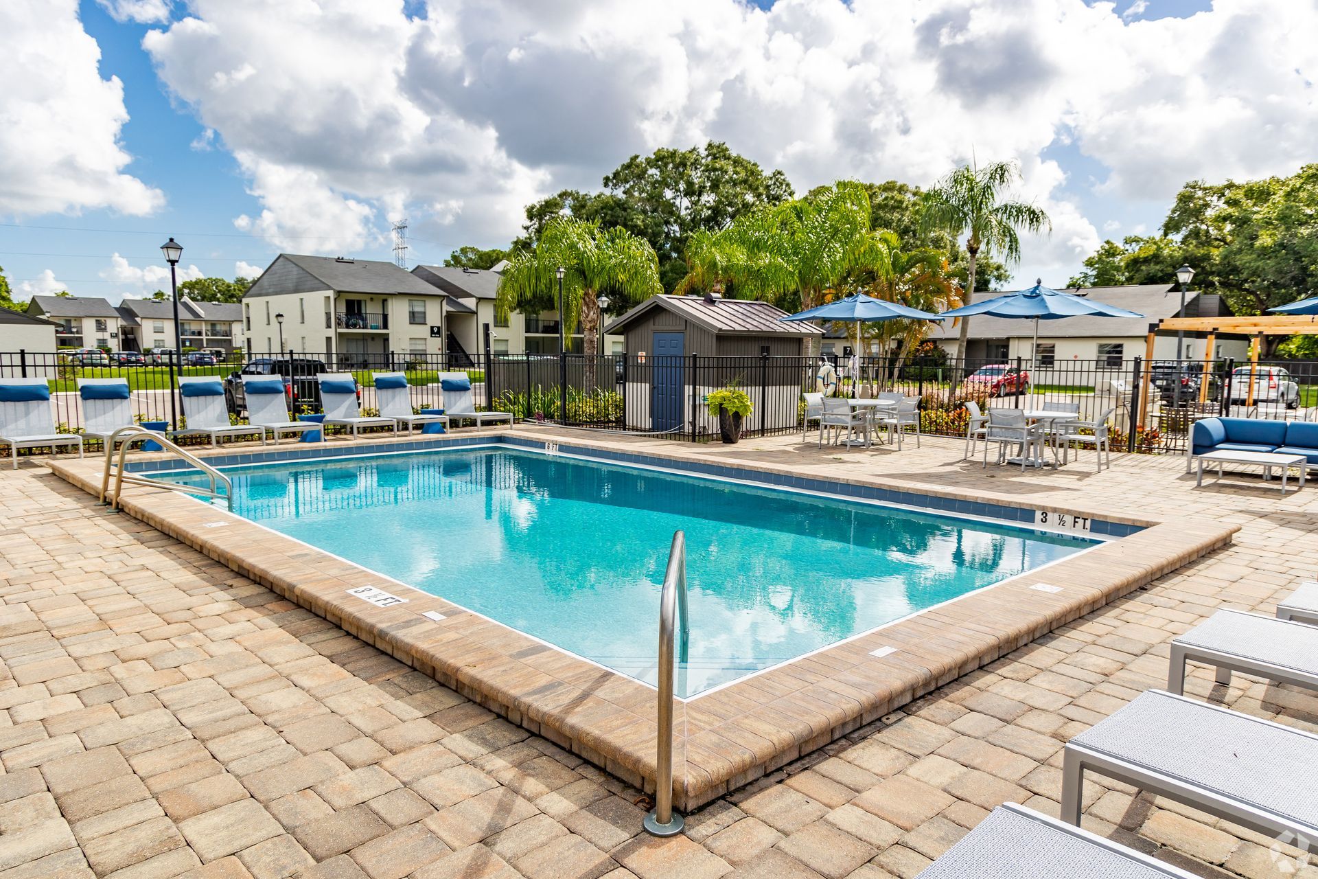 Outdoor swimming pool with lounge chairs, umbrellas, and cabanas under a sunny sky