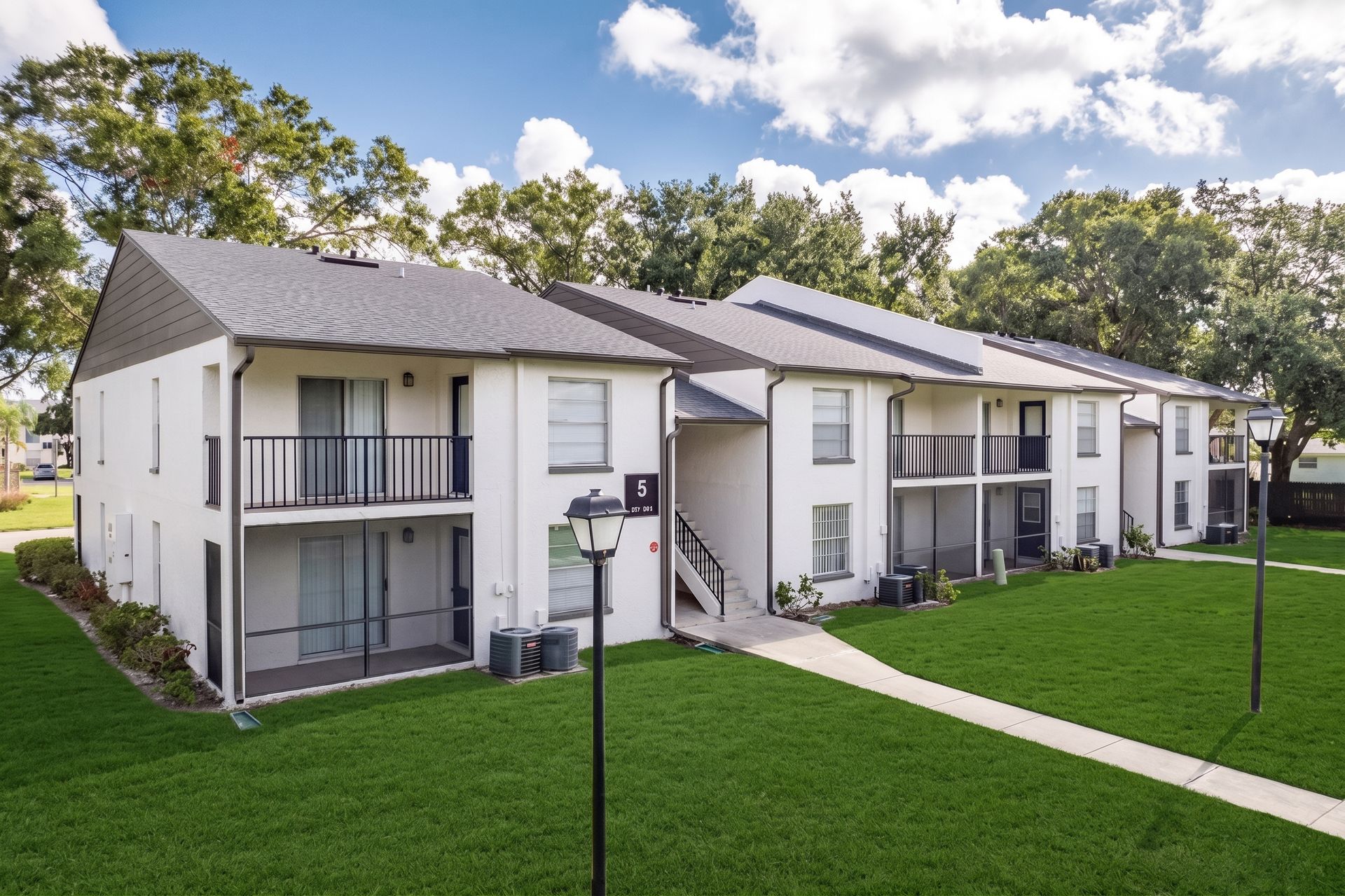 Two-story apartment building with balconies, stairs, and a green lawn under a blue sky