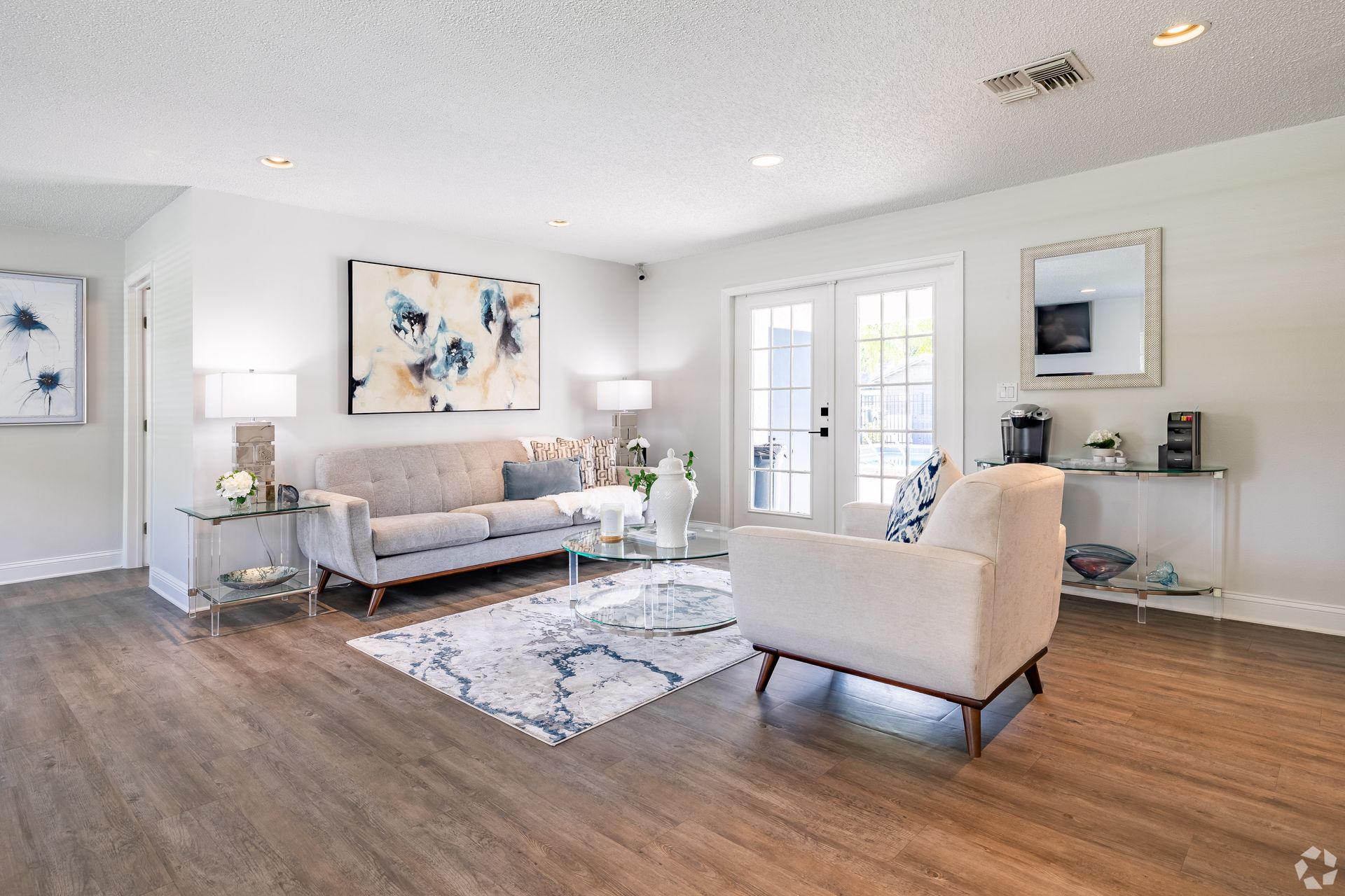 Bright modern living room with gray sofa, cream chair, coffee table, wall art, and French doors