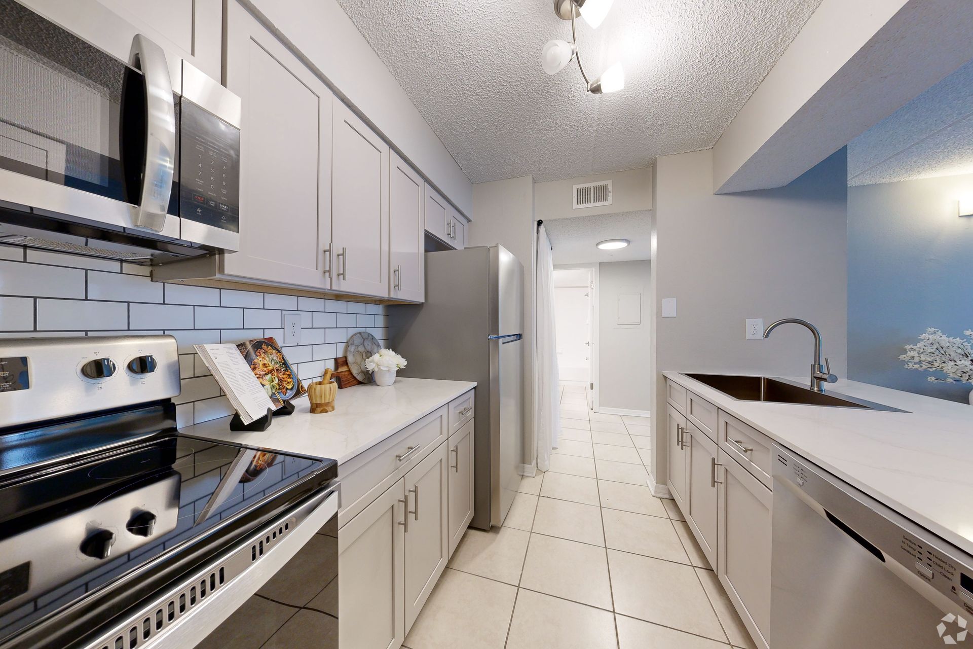 Bright modern galley kitchen with white cabinets, stainless appliances, and a sink by the window