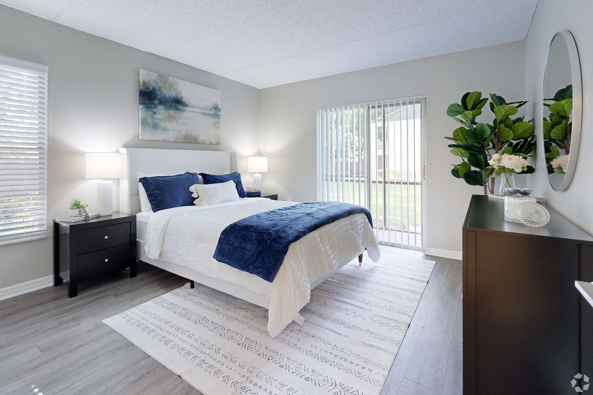 Bright modern bedroom with a white bed, navy accents, gray walls, and large windows.