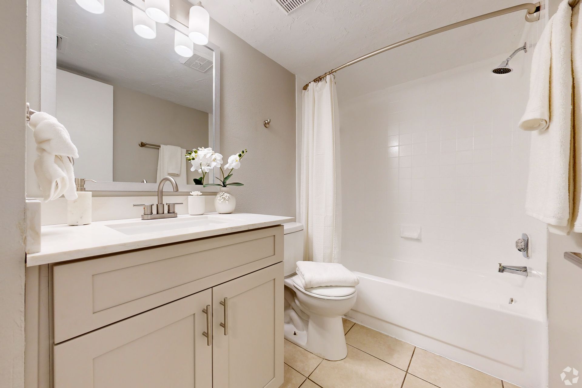 Bright white bathroom with vanity, mirror, flowers, and tub-shower combo