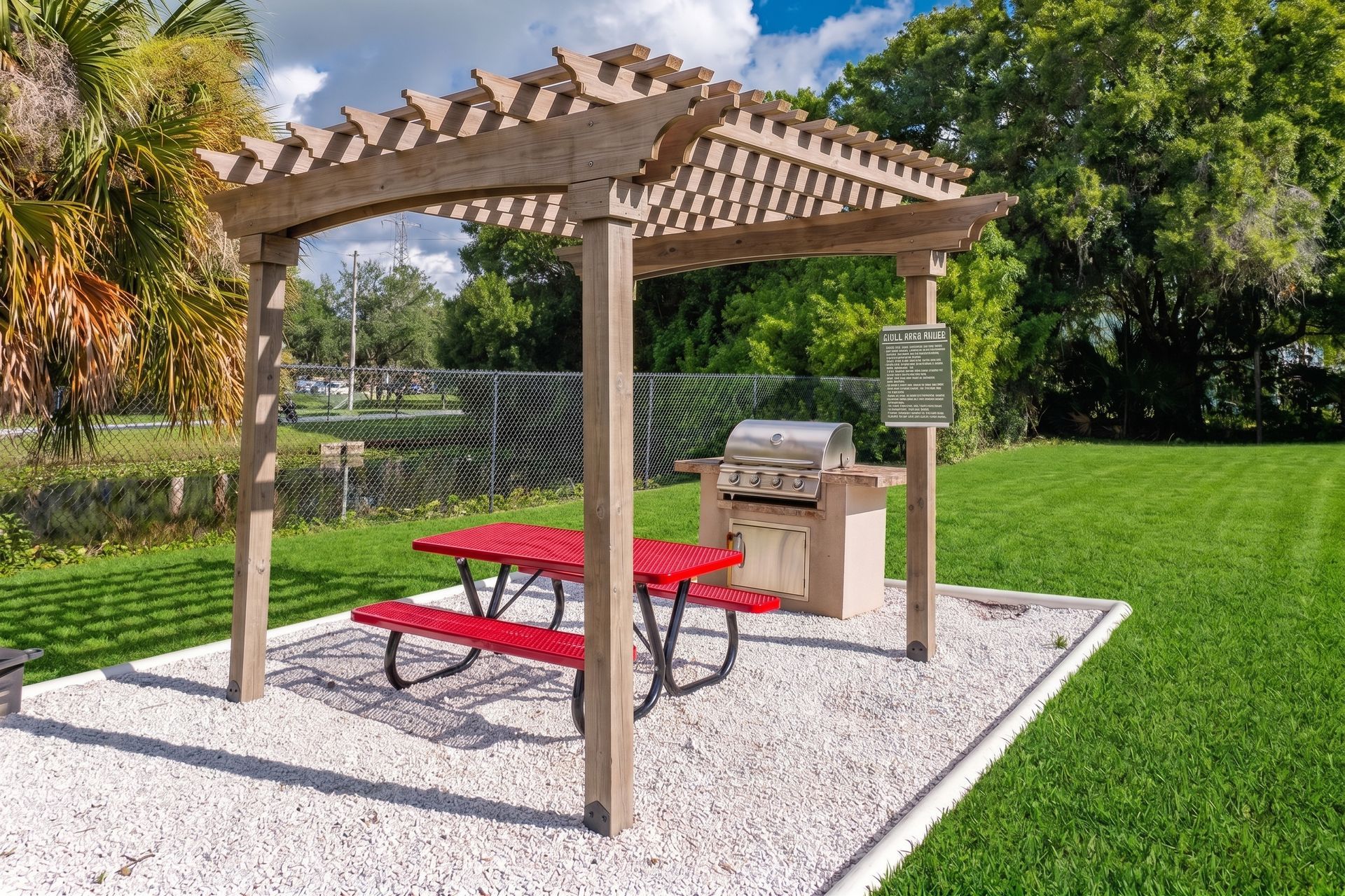 Outdoor picnic shelter with red table, grill, and stone path beside a lake