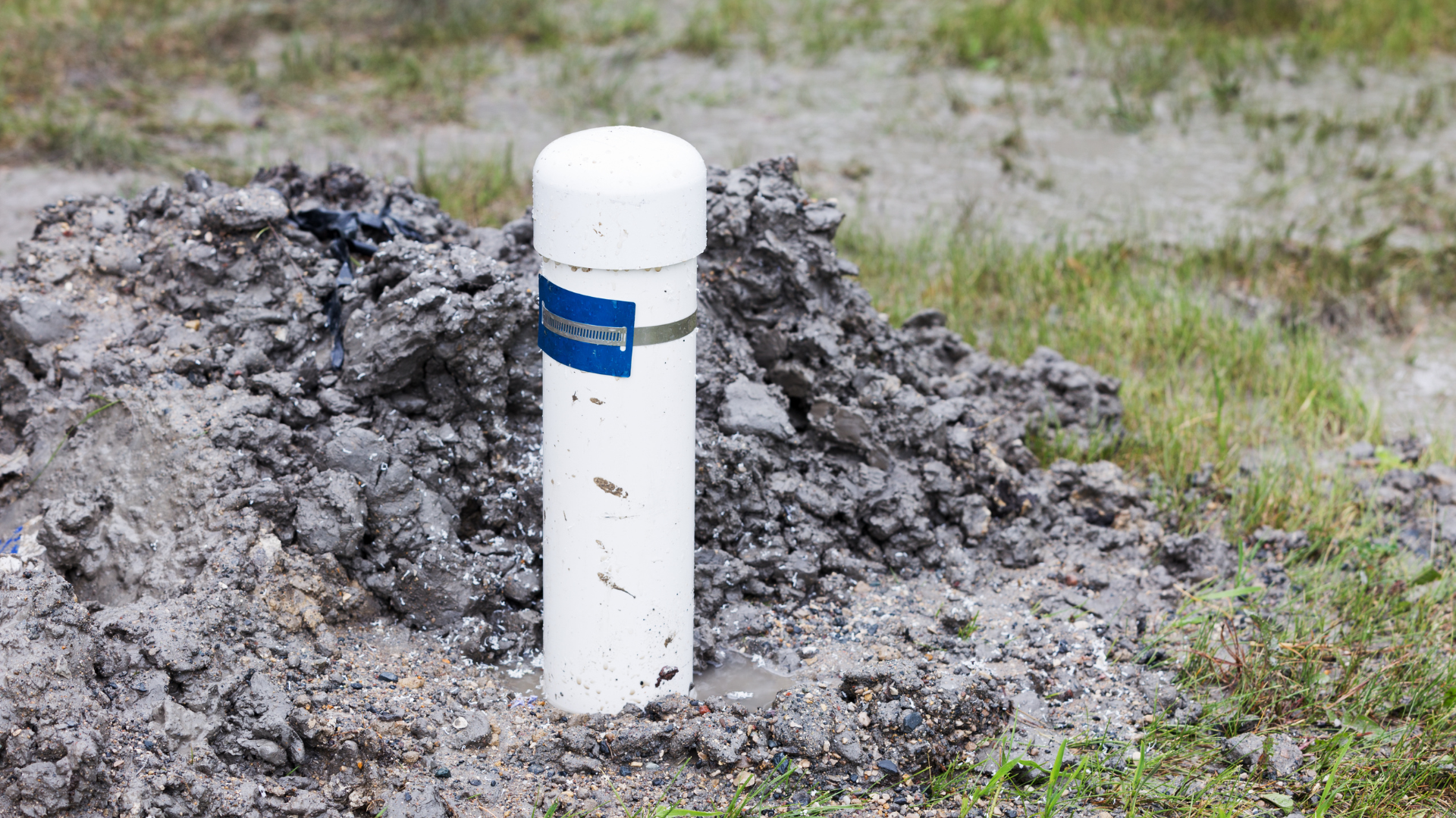 A white PVC pipe capped at the top, standing upright in a pile of dirt and gravel in an outdoor area.