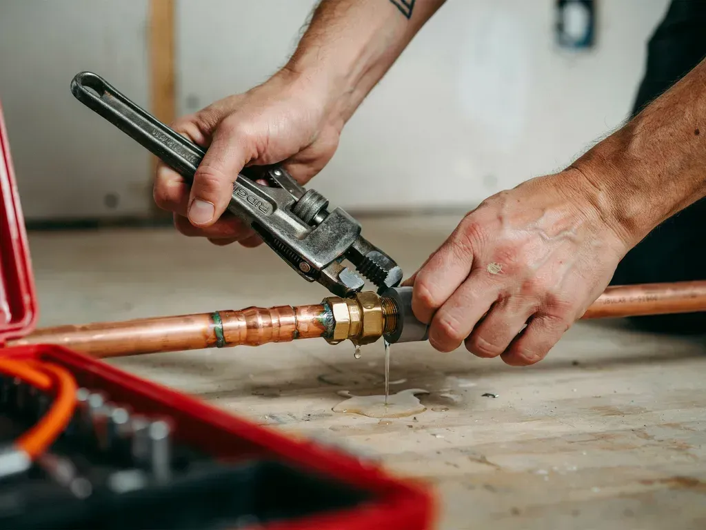 Hands using a pipe wrench on a copper pipe during plumbing repair