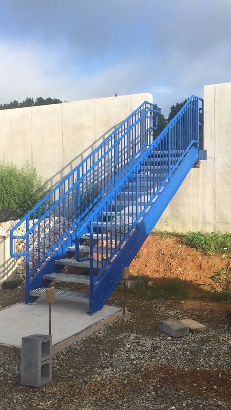 Blue metal exterior staircase against a concrete wall, leading upwards from a concrete base.