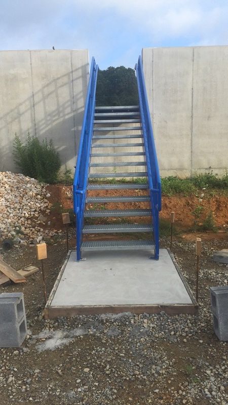 Blue metal staircase leading up to a concrete wall, set in an unfinished outdoor area.