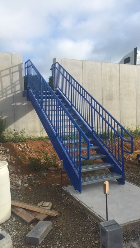 Blue metal staircase against a concrete wall, leading up; on a concrete pad.