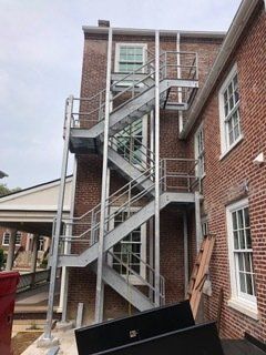 Exterior metal fire escape on a brick building, with windows.