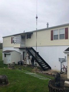 Mobile home exterior with a long pole extending upwards; dark stairs and small shed below.
