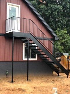 Black metal exterior staircase leading to a door and landing on a red-sided building.