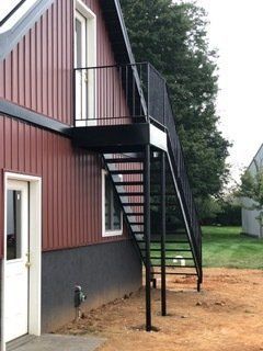 Exterior view of a burgundy house with a black metal staircase leading to a small balcony.