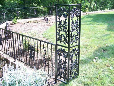 Black decorative metal fence with floral design near a garden and lawn.