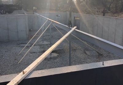 Steel beams being placed in a concrete foundation pit for construction.