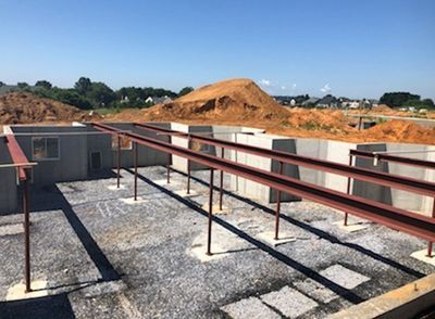 Steel beams supported by posts over a gravel foundation within concrete walls at a construction site.