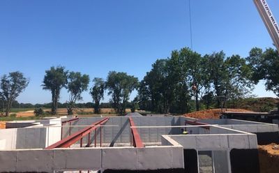 Construction site with concrete foundation and steel beams, clear blue sky, trees in the background.