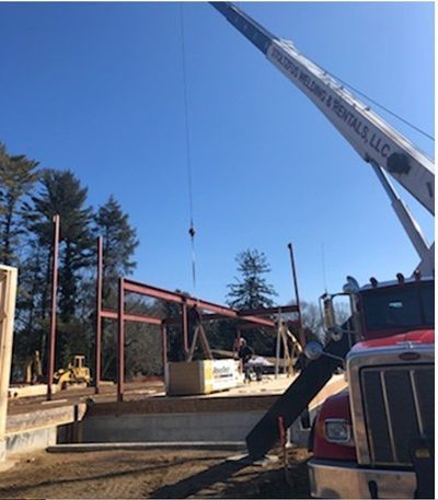 Construction site with a crane lifting a steel beam; sunny, blue sky.