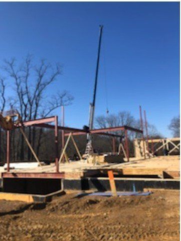 Construction site with a crane lifting steel beams; sunny day, blue sky.