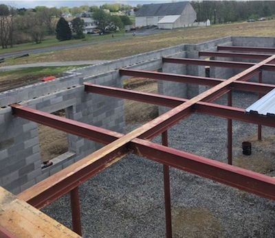 Steel beams crisscross atop a concrete block foundation, a building under construction outdoors.