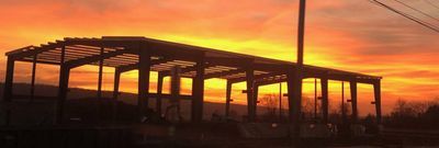 Silhouette of a building structure against a vibrant orange and yellow sunset sky.