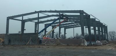 Steel structure of a building under construction on a cloudy day, with a boom lift.