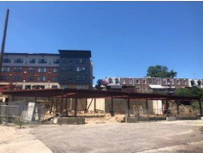 Construction site with exposed steel framework, adjacent to existing buildings under a blue sky.