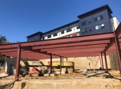 Construction site with a steel framework; modern apartment building in background.