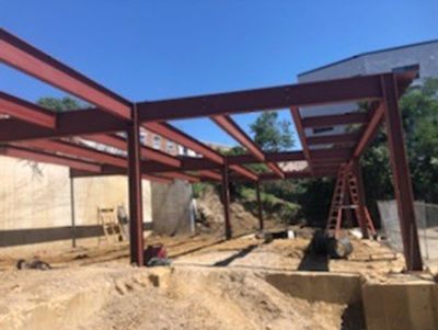 Steel framework of a building under construction, painted red, against a blue sky.
