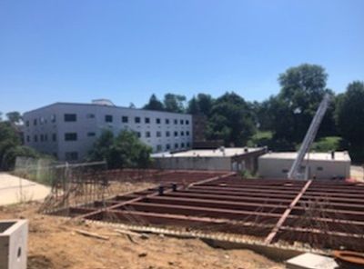 Construction site with a partially built foundation in front of a multi-story white building under a blue sky.