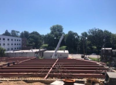 Construction site with steel beams, crane, and buildings under a blue sky.