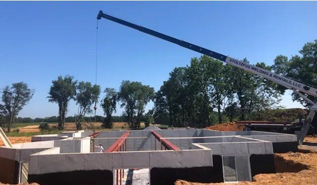 Crane lifting beams over a concrete foundation on a construction site, blue sky in background.