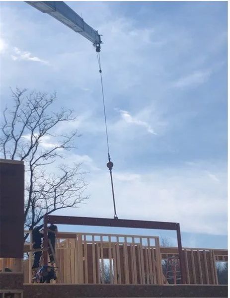 Crane lifting a wooden wall frame during a house construction on a sunny day.