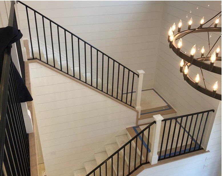 Staircase with black metal railings, white walls, and a large chandelier.