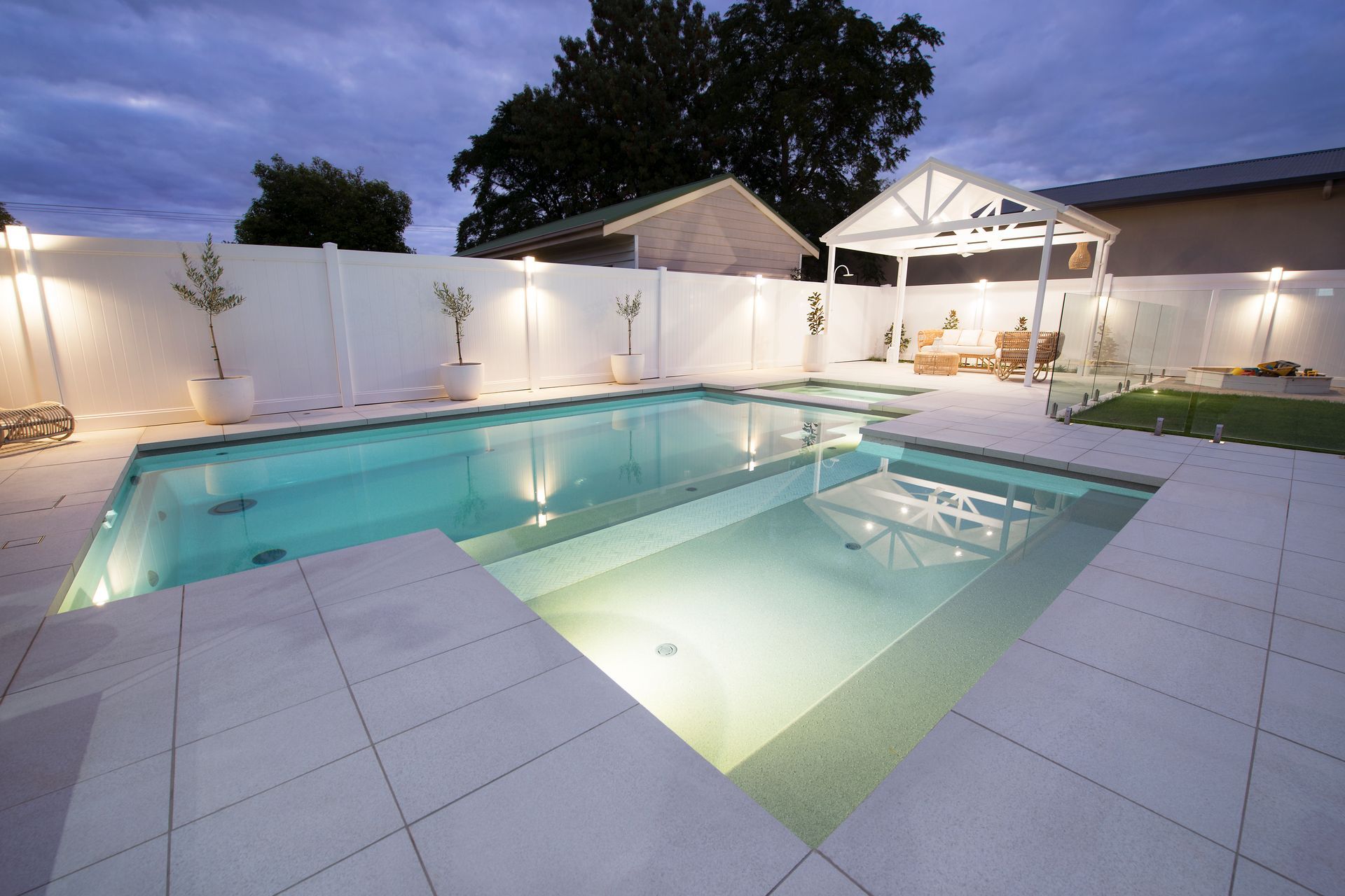 Backyard pool at dusk with white walls, lights, and a gazebo — Swan Hill Pool & Spa Centre in Swan Hill, VIC