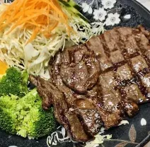 Grilled steak with broccoli, shredded salad, and orange slices on a black plate