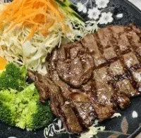 Grilled steak with broccoli, shredded salad, and orange slices on a black plate