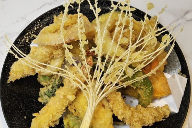 Fried shrimp tempura piled on a black plate, topped with thin crispy strands