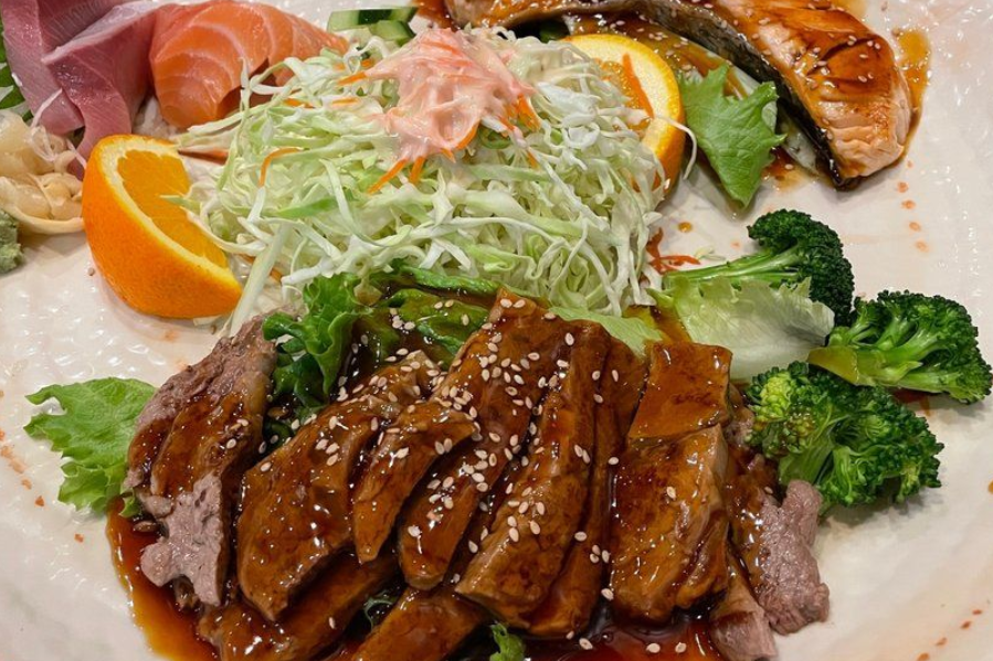Plated Japanese meal with glazed meat, sushi, orange slices, salad, and broccoli