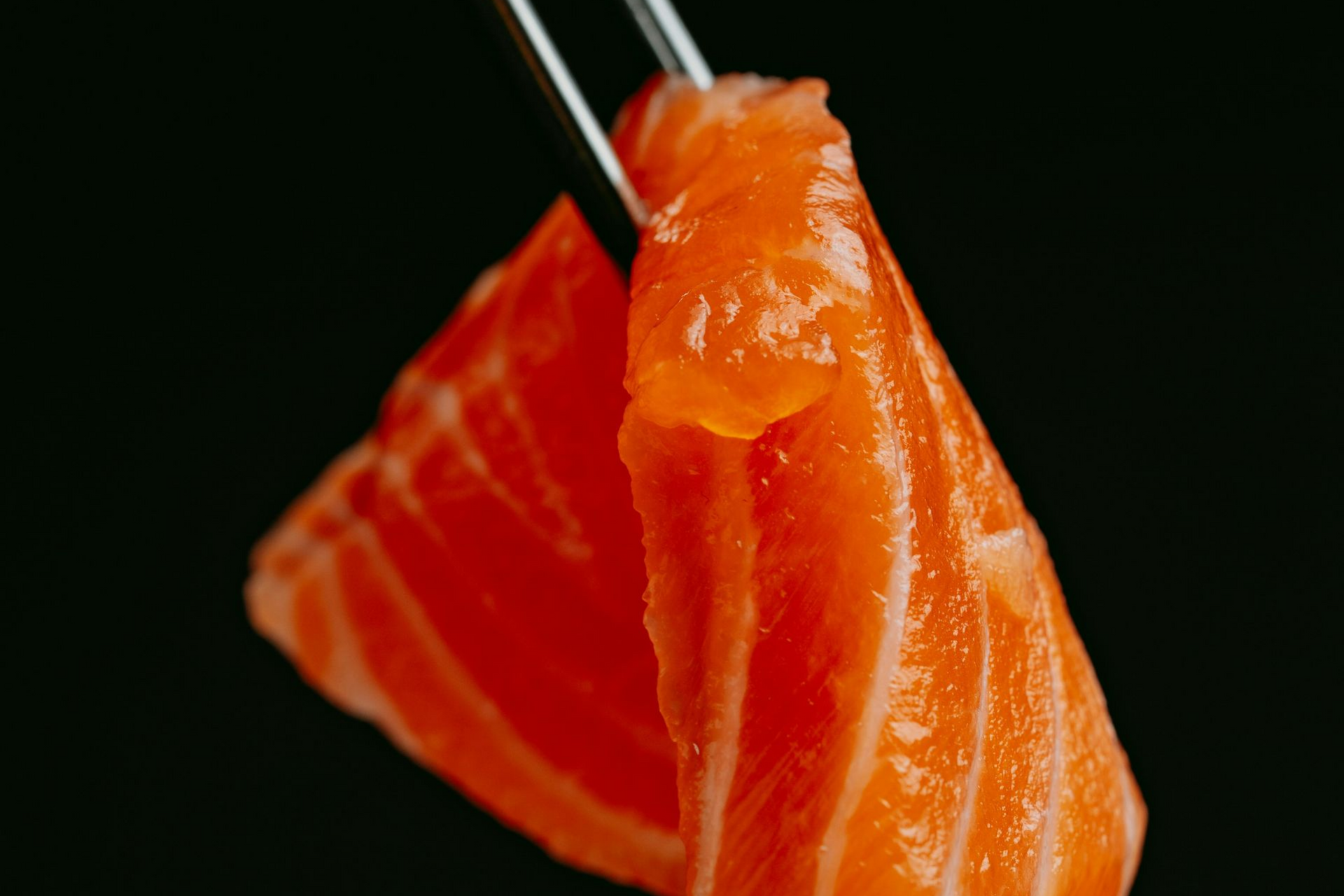 Close-up of orange salmon sushi held with chopsticks against a black background