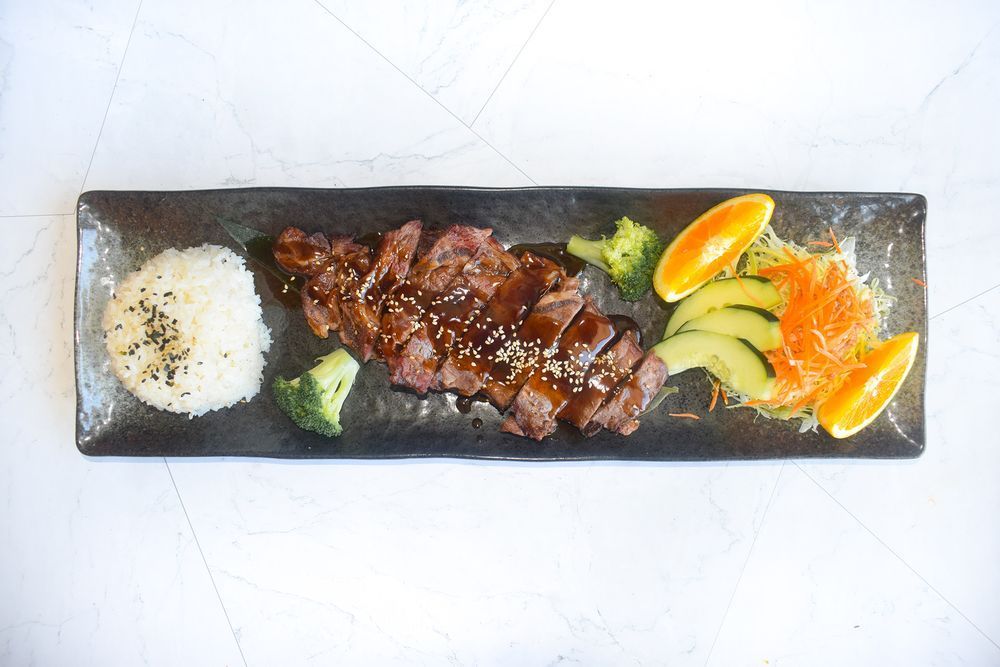 Grilled steak with rice, avocado, and orange slices on a long black plate