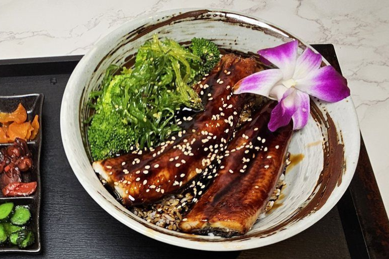 Grilled glazed fish bowl with seaweed, sesame seeds, and purple orchid garnish