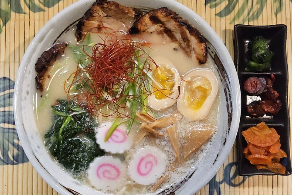 Japanese ramen bowl with sliced pork, soft-boiled egg, spinach, narutomaki, and side dishes
