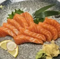 Sliced salmon sashimi on a gray plate with lemon, wasabi, and a purple orchid garnish