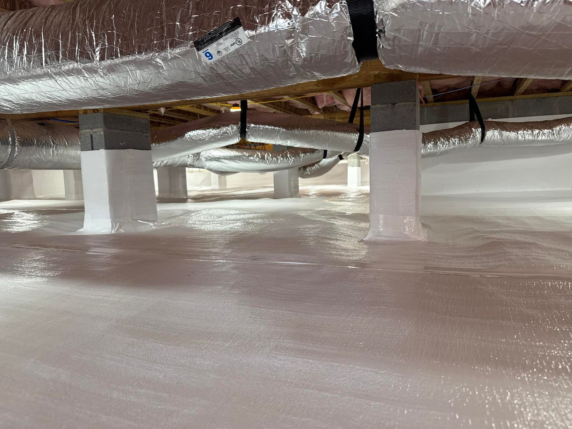 A clean, encapsulated crawl space with white moisture barrier lining the floor and up the concrete support piers.