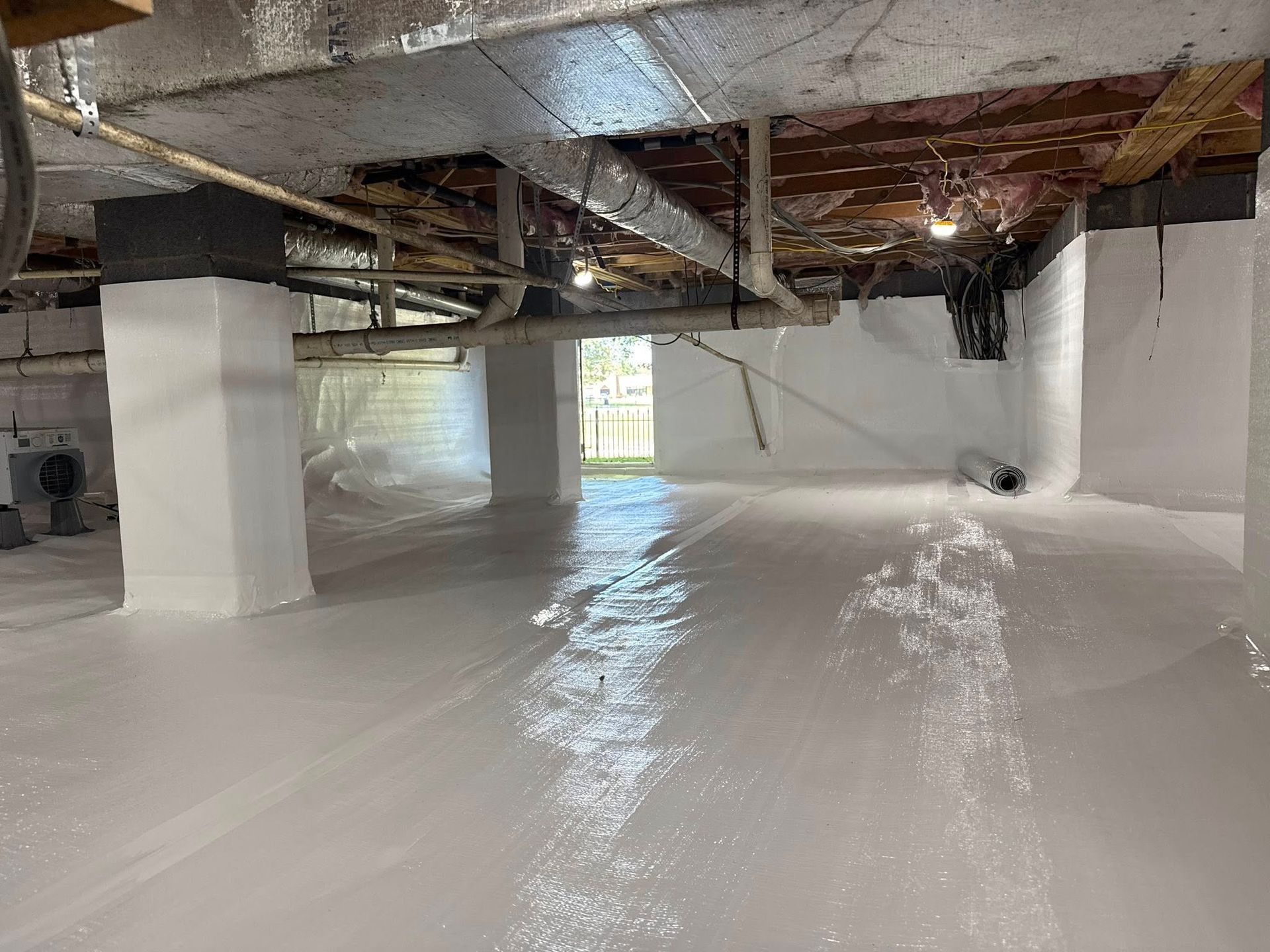 A clean crawl space with white vapor barrier covering the floor and foundation walls, featuring exposed joists above.