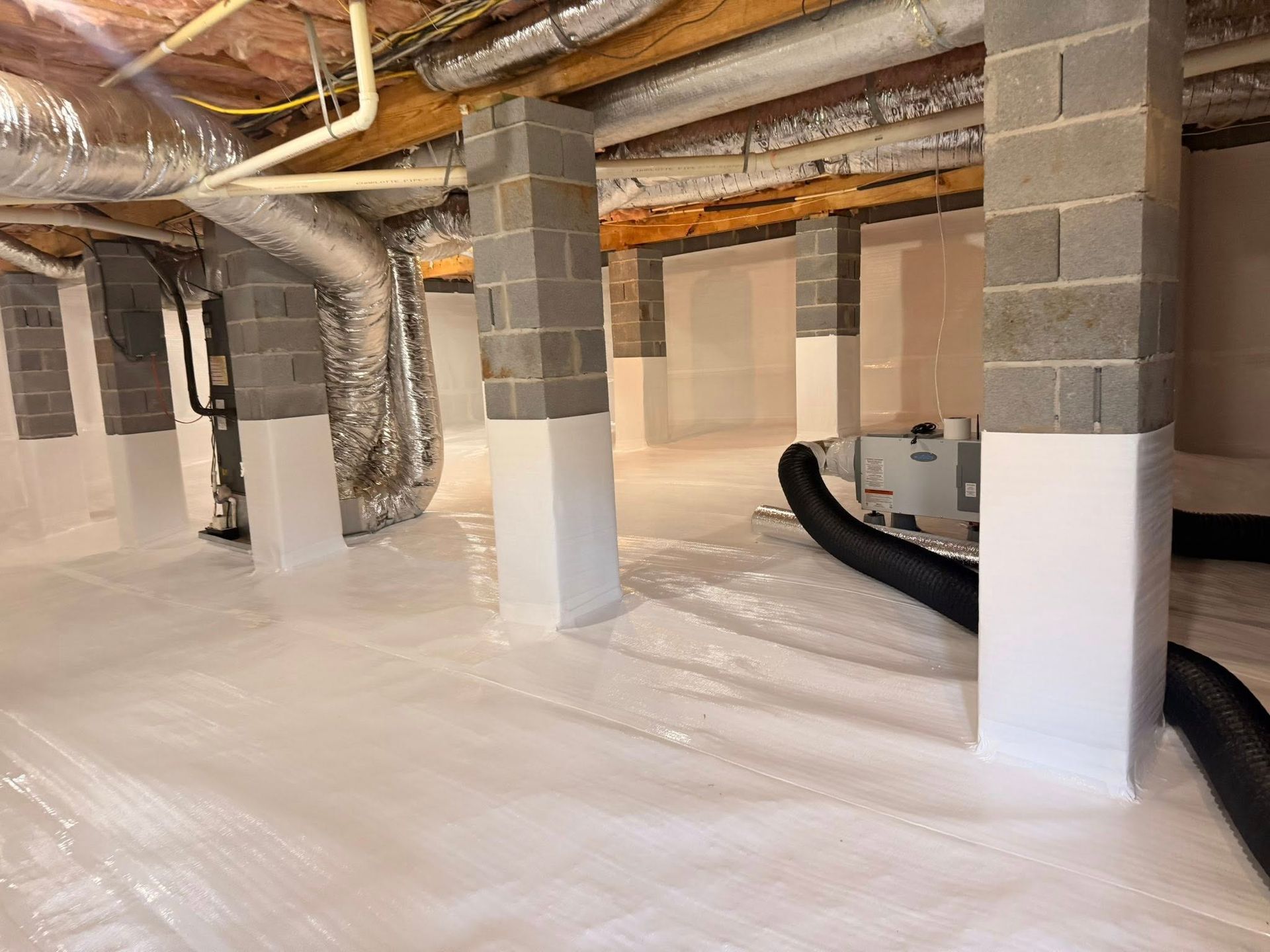 A crawl space with a clean white vapor barrier, encapsulated concrete pillars, and a dehumidifier system.