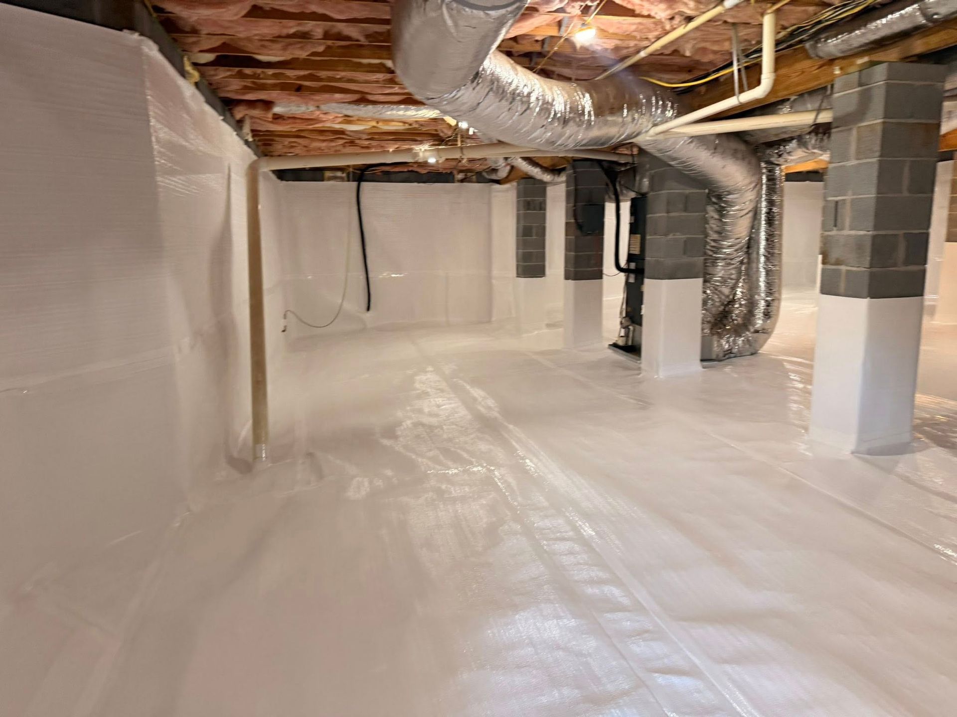 A clean crawl space with white vapor barrier sheeting on the walls and floor, supported by gray concrete pillars.