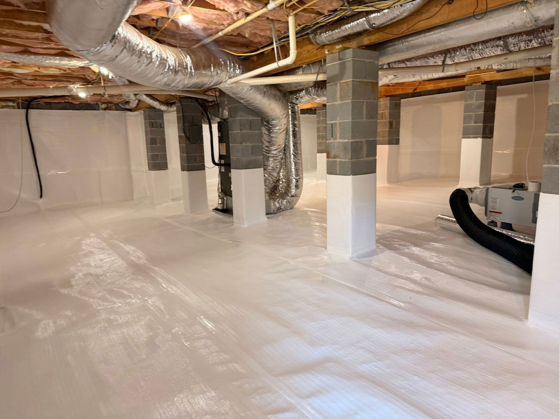 A clean crawl space with white vapor barrier covering the floor and lower walls, supported by concrete pillars.