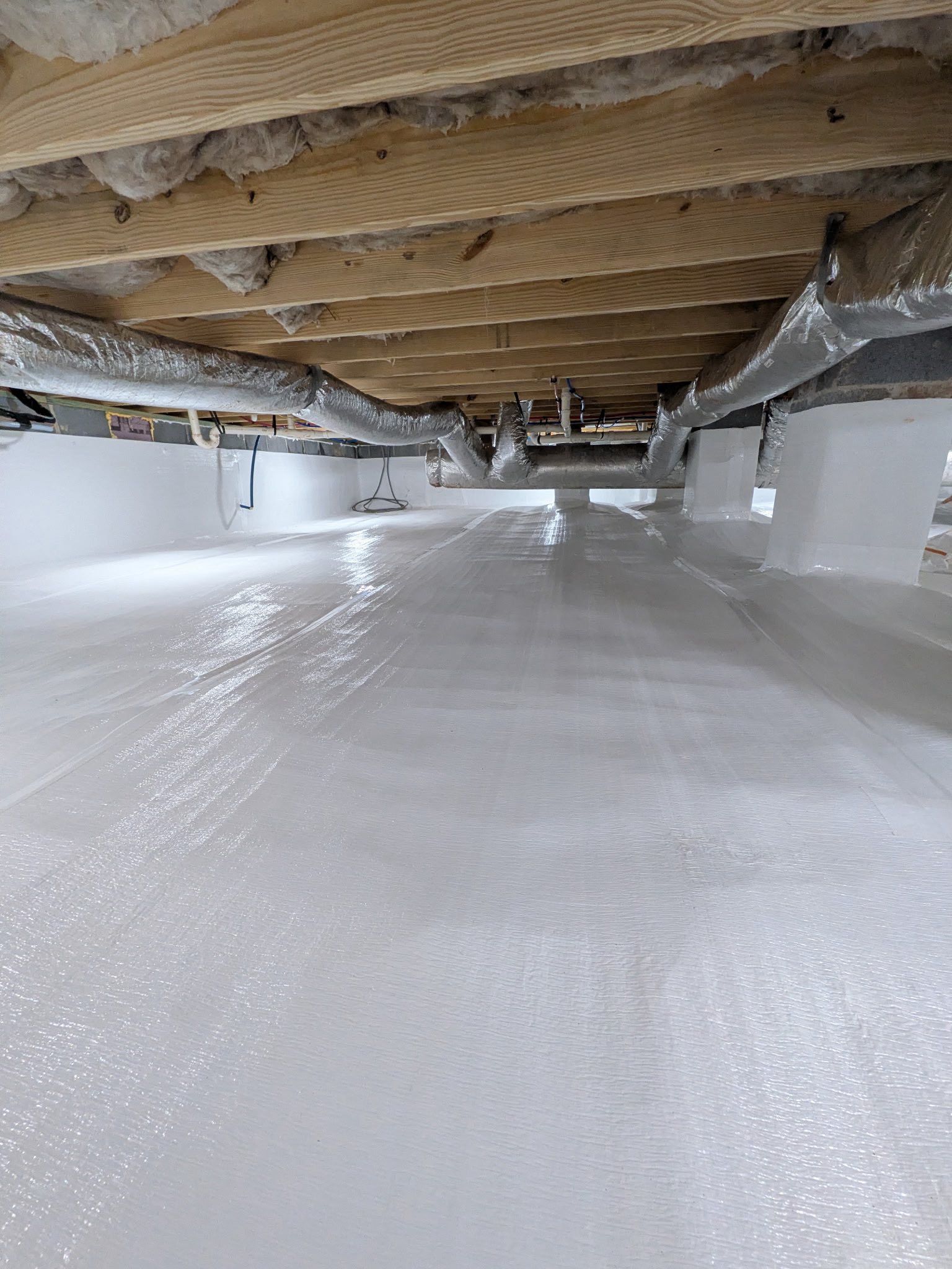 Crawl space with a white vapor barrier on the floor, exposed floor joists above, and silver HVAC ductwork.
